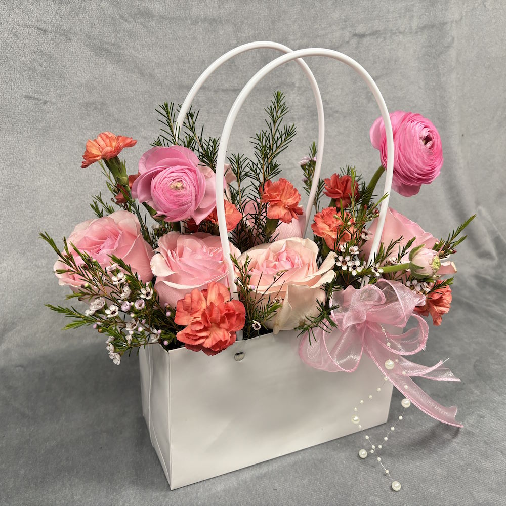 pink roses and orange carnations with waxflowers in gift bag